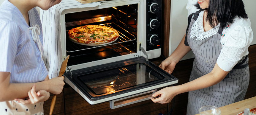 Crop women putting pizza in oven